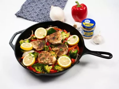 Skillet with seasoned chicken and vegetables, garnished with lemon, ready for a delicious meal