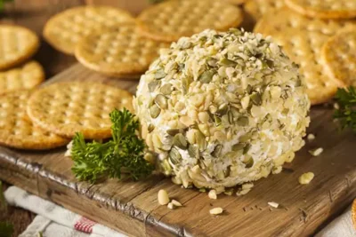 Cheese ball rolled in nuts and seeds, served with crackers on a wooden tray, perfect for appetizers and gatherings