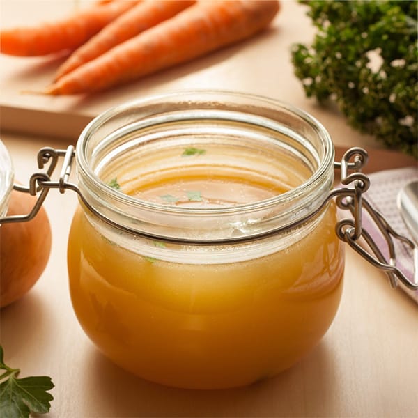 Rich broth made from onion in a glass jar, with onion and other ingredients in the background.