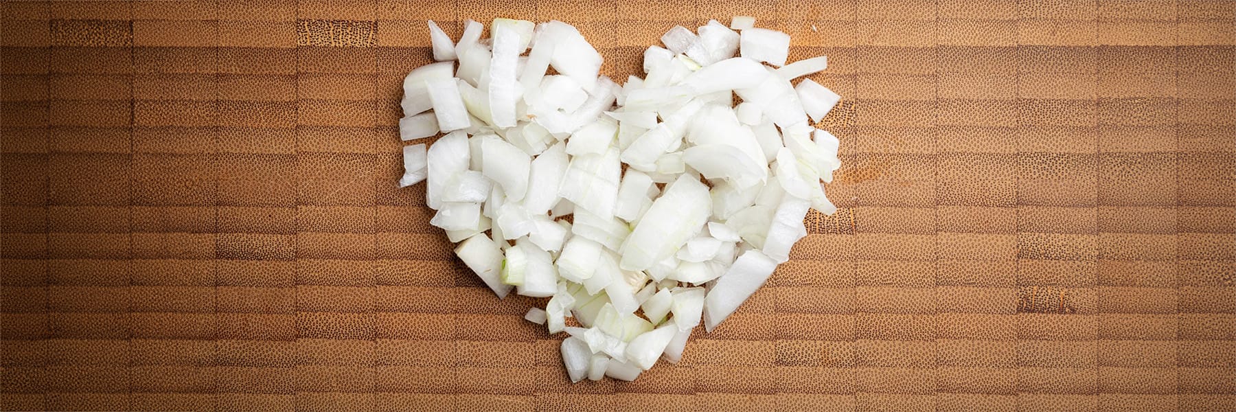 Heart shape made of diced, white onion on a bamboo cutting board background.