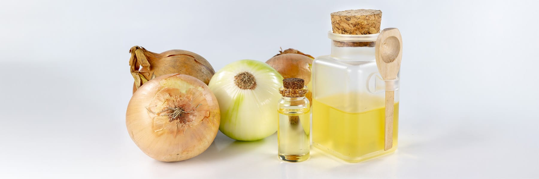 Bottles of healthy natural medicine made from onion with yellow onion in the background on a white backdrop.