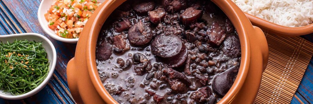 Brazilian feijoada with sides of rice, greens, and diced tomatoes