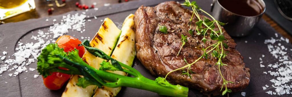 Grilled steak with vegetables and sauce on a slate board, an appetizing meal setup