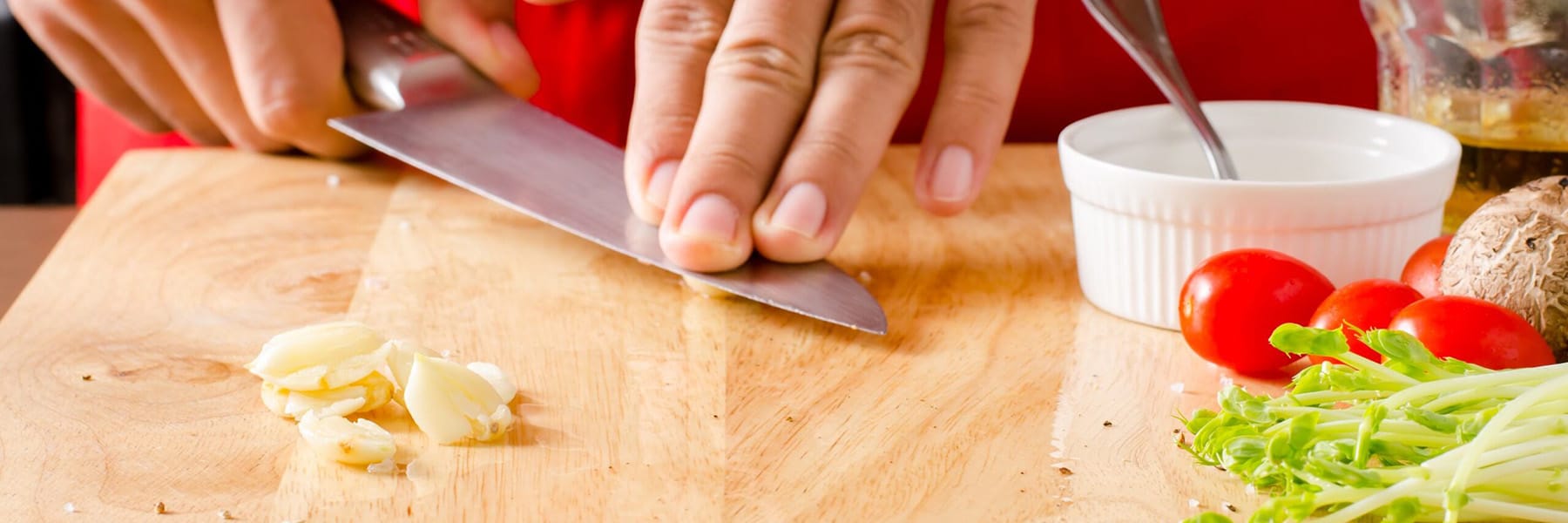 Person slicing garlic on a cutting board, preparing fresh ingredients for cooking