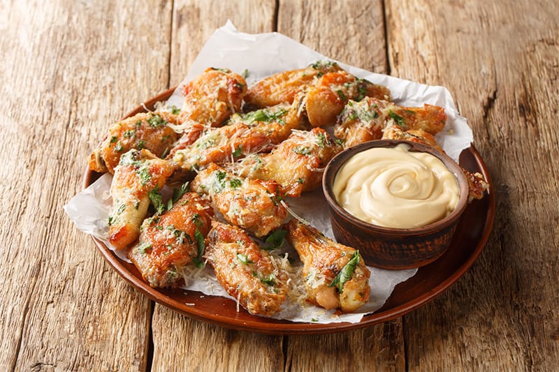 Garlic Parmesan chicken wings topped with herbs and grated cheese, served with a creamy dipping sauce.