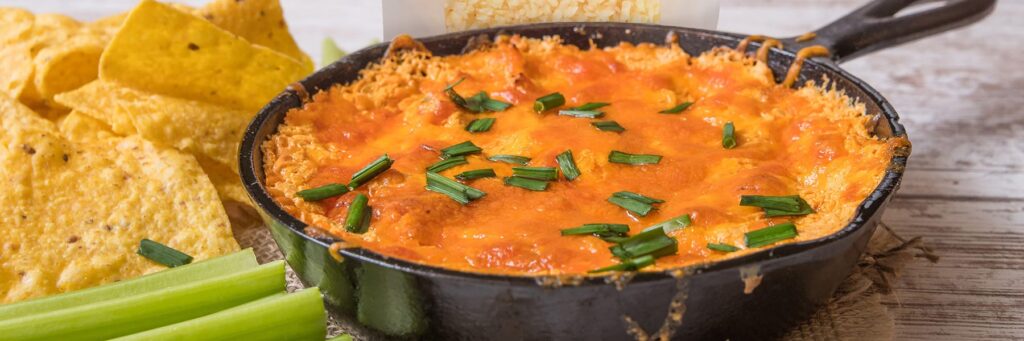 Cheesy dip in a skillet with tortilla chips and veggie sticks, perfect for snacking