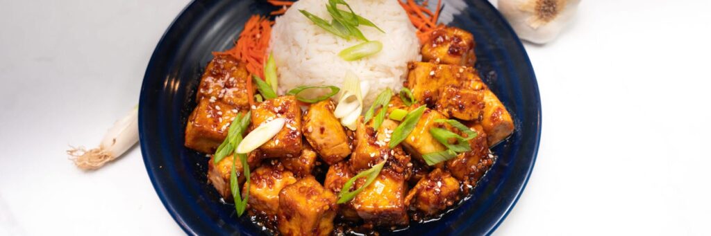 Plate of glazed tofu with rice and carrots, garnished with green onions and sesame seeds