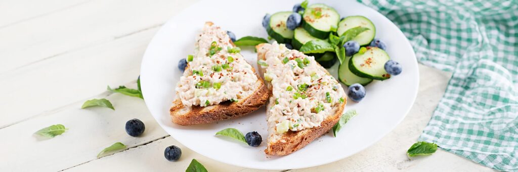 Plate of creamy shrimp toast with garnished cucumber slices and blueberries on a white table