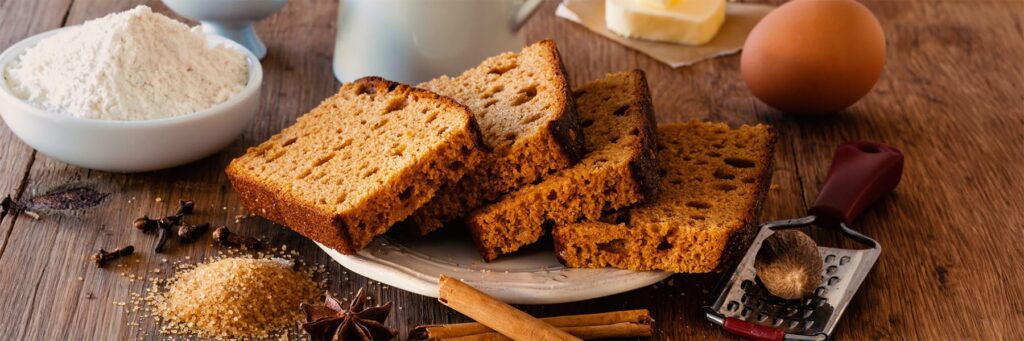 Freshly baked spice bread slices served with ingredients like flour, sugar, and cinnamon on a wooden table