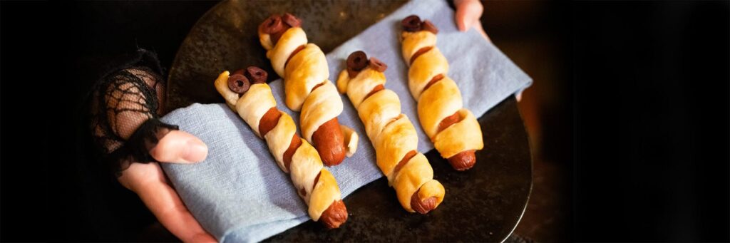 Hand serving creatively wrapped hot dogs on a plate for a tasty snack