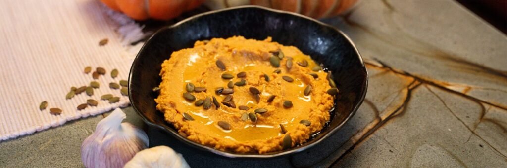 Pumpkin puree in a skillet topped with seeds and oil, surrounded by rustic kitchen elements
