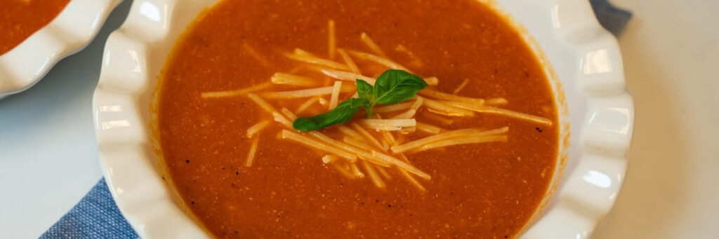 A bowl of tomato soup garnished with cheese and basil, served in a white dish
