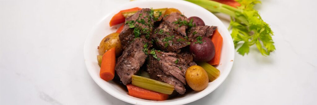 Plated beef stew with carrots, celery, potatoes and garnished with parsley on a white background