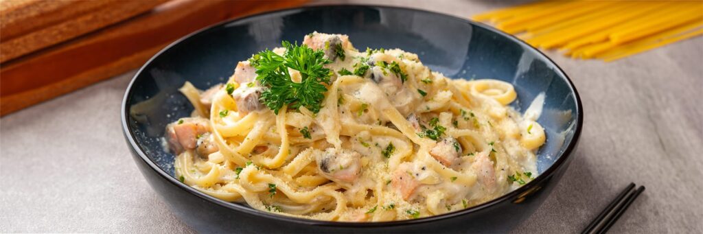 Creamy pasta with salmon and herbs in a blue bowl, ready to serve