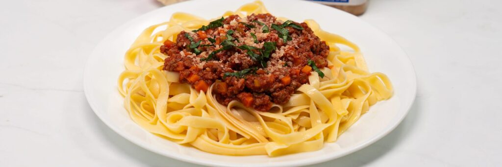 Plate of fettuccine pasta topped with a rich Bolognese sauce and garnished with fresh herbs