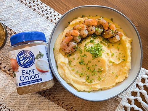 Bowl of shrimp and grits garnished with herbs beside a container of onion spice