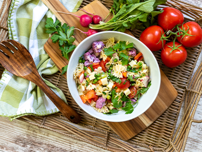 Bright, appetizing bowl of pasta salad with fresh vegetables, cheese, and herbs on a wooden table
