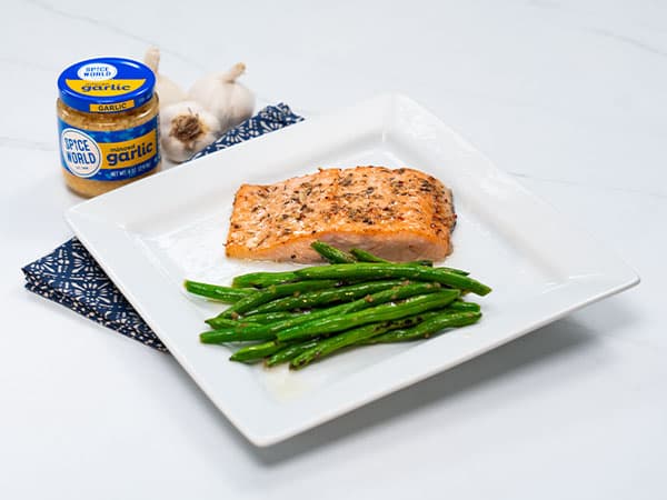 Grilled salmon and green beans on a white plate, with garlic seasoning