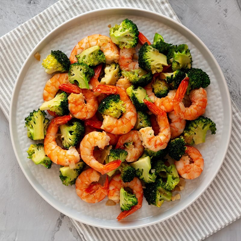 Healthy shrimp and broccoli dish served in a white bowl on a striped napkin
