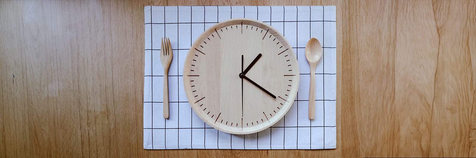 Wooden clock plate on a table mat with a fork and spoon, symbolizing time to eat