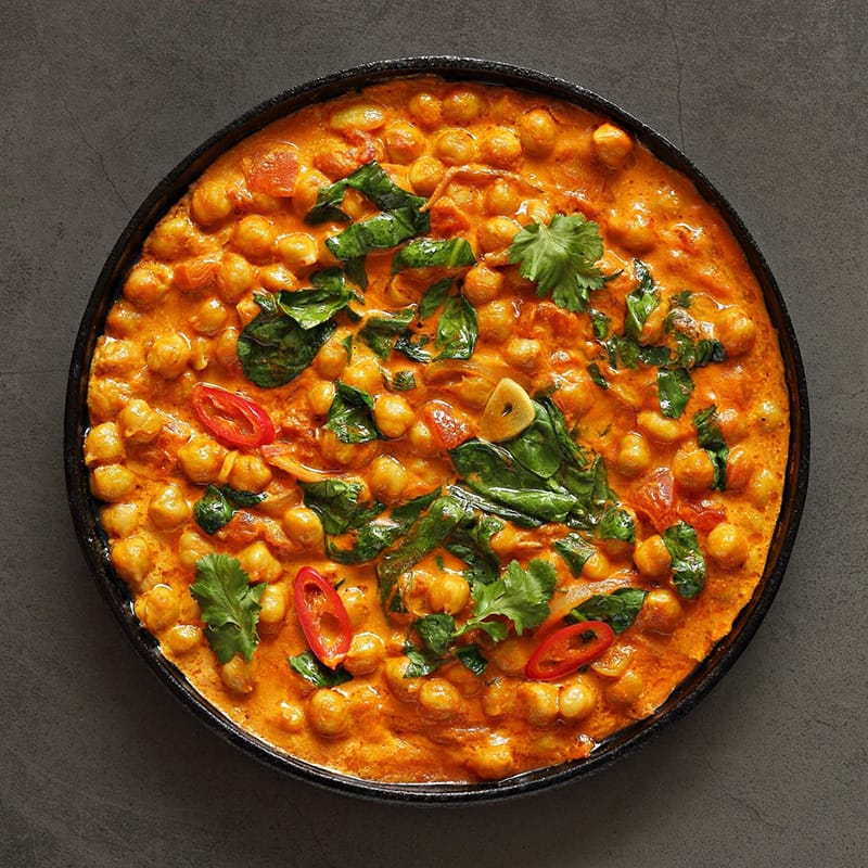 Top view of a spicy chickpea curry garnished with herbs in a skillet