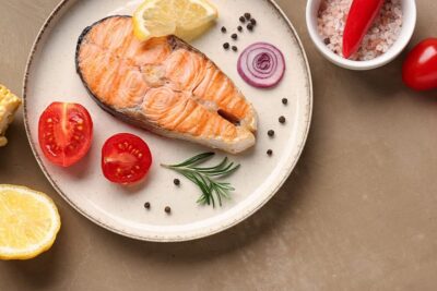 Grilled salmon fillet with lemon and tomatoes on a plate, showcasing a healthy meal