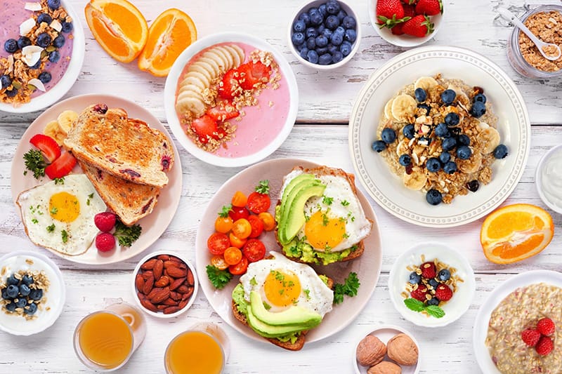 Assorted healthy breakfast dishes with fruits, eggs, and oats laid out on a wooden table