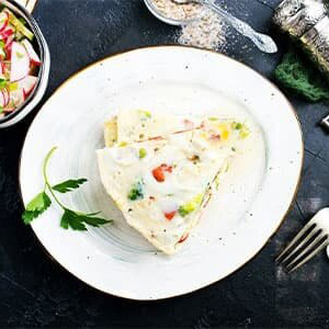 Overhead view of an egg white omelette full of veggies on a white plate on a dark counter.