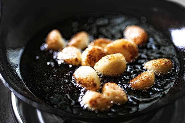 Garlic cloves frying in oil in a black skillet