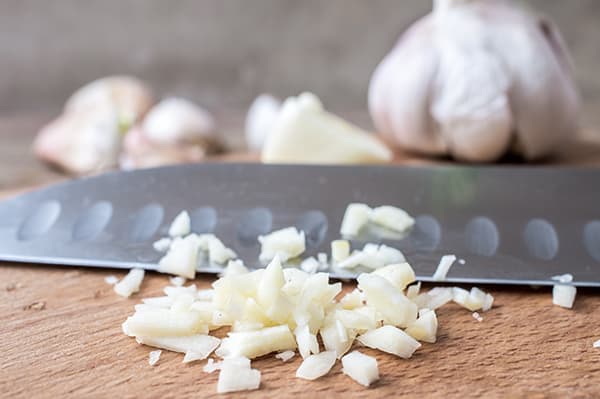 Garlic cloves chopped on a cutting board with a knife, prepped for cooking