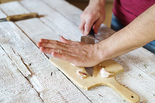 Person slicing garlic on a wooden cutting board, preparing food