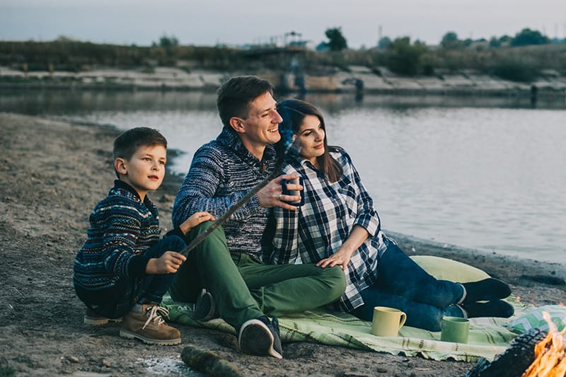 Family enjoying a picnic with marshmallows by a lakeside campfire