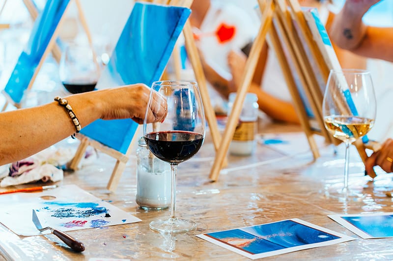 Person enjoying a glass of red wine during an artistic painting class