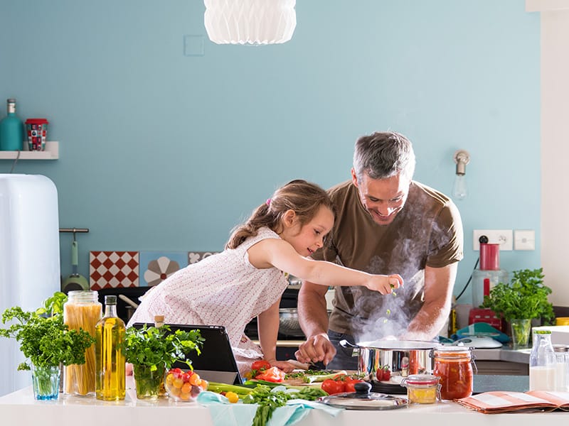 Man and child cooking together in a bright kitchen, preparing a healthy meal