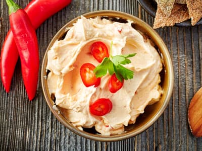 Bowl of creamy hummus topped with tomatoes and herbs, served with crispbread and chili peppers