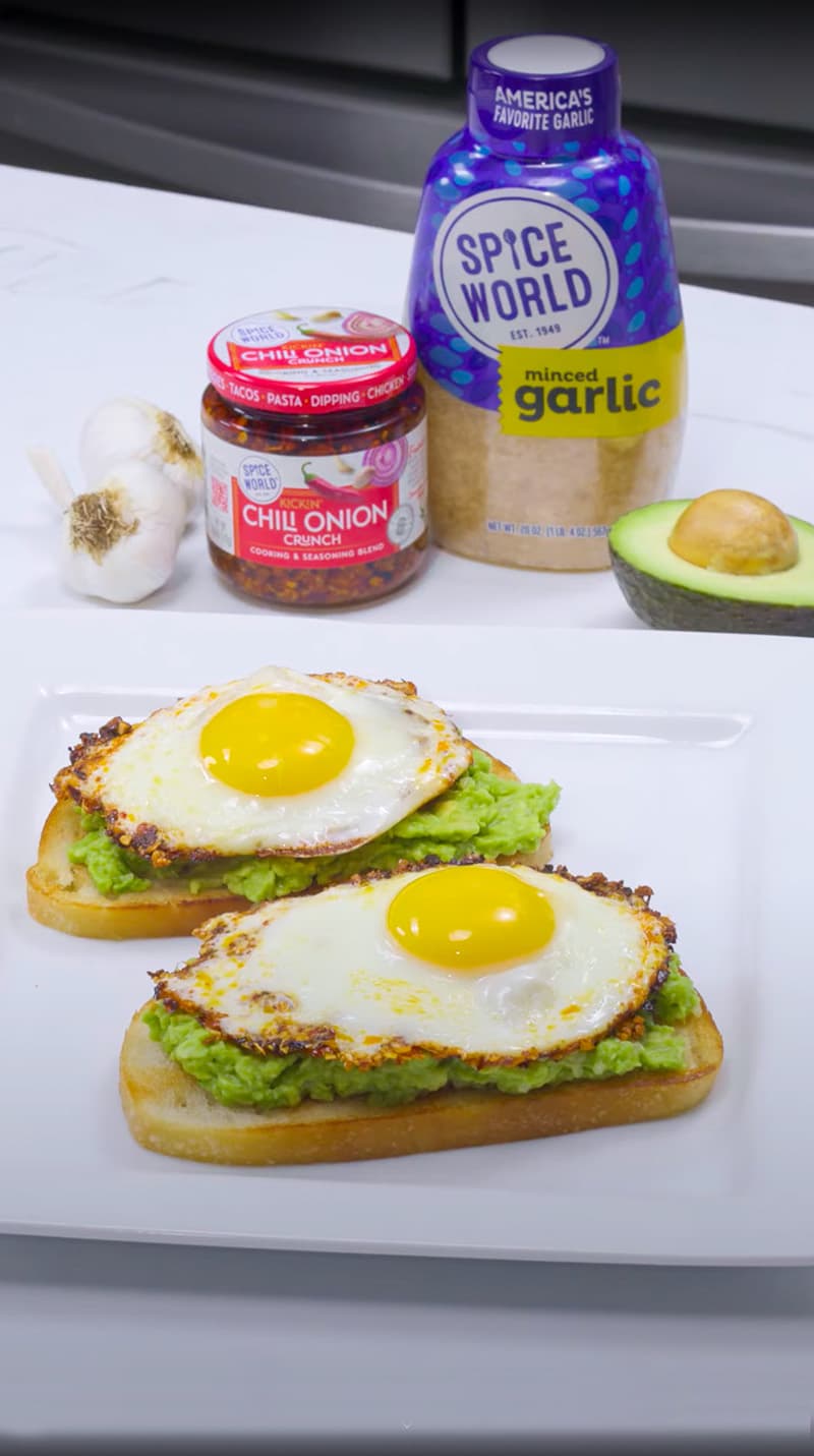 Avocado toast topped with fried eggs and seasoning ingredients like garlic and chili onion in the background