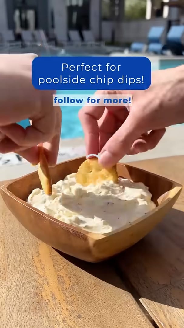 Hands dipping chips into a creamy dip at a poolside setting