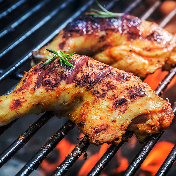 Grilled chicken legs on a barbecue with flames and rosemary sprigs