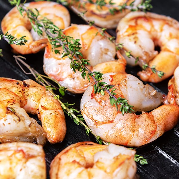 Grilled shrimp garnished with thyme on a black skillet