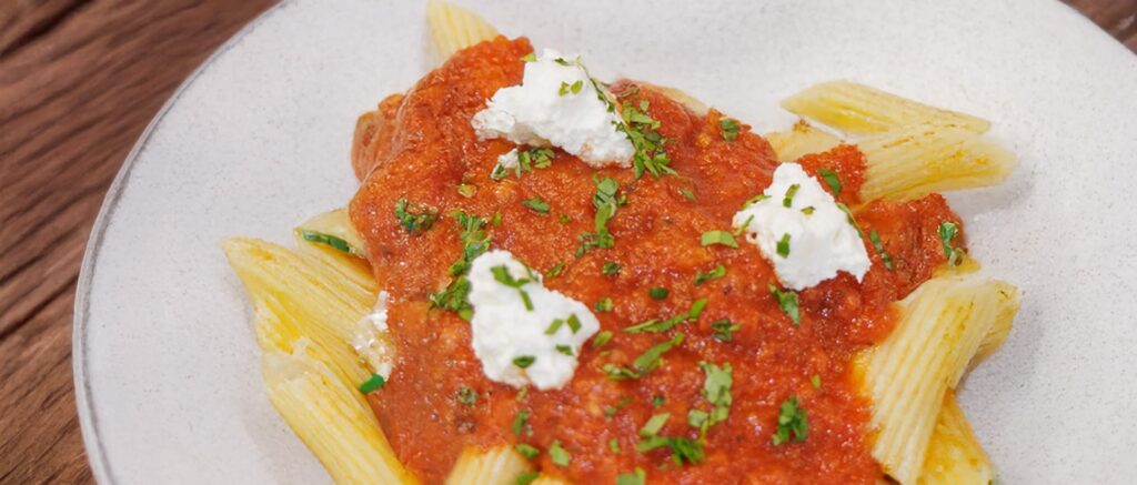 Penne pasta with tomato sauce and dollops of ricotta, garnished with herbs