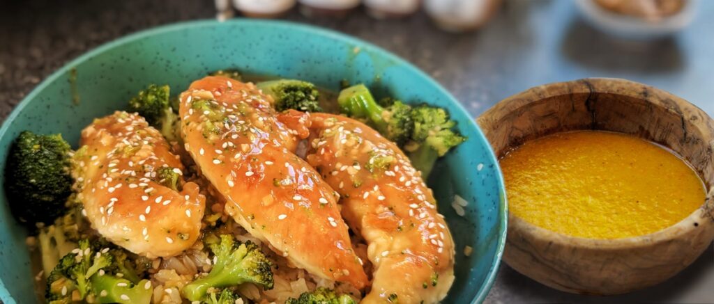 Bowl of teriyaki chicken with broccoli and rice, served with a side of sauce