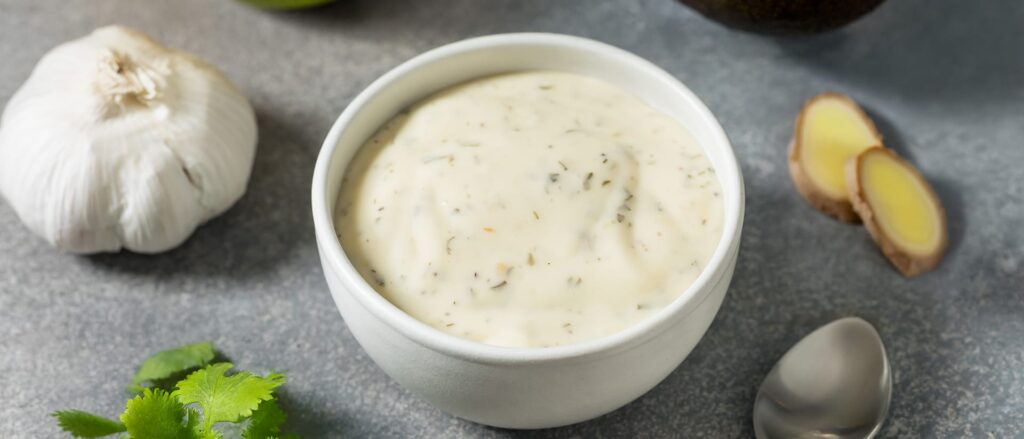 Bowl of creamy garlic sauce with fresh garlic and ginger on a kitchen counter
