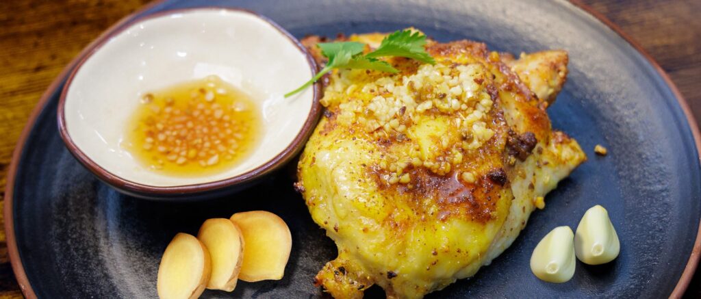 Grilled chicken thigh with garlic sauce and sliced ginger on a dark plate