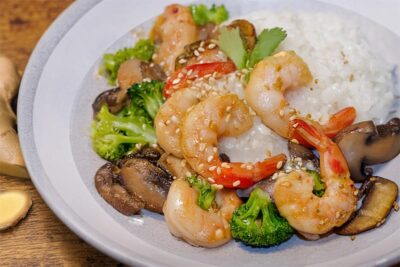 Plate of shrimp stir-fry with rice, broccoli, and mushrooms, garnished with sesame seeds