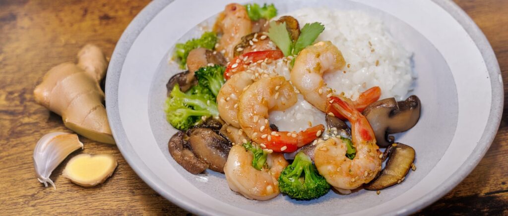 Plate of shrimp stir-fry with broccoli, mushrooms, and rice garnished with sesame seeds