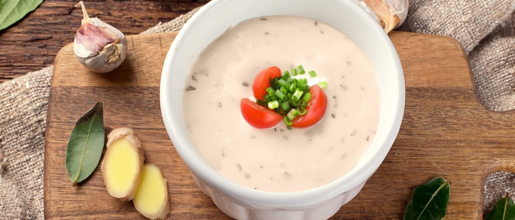 Bowl of creamy soup garnished with tomatoes and green onions on a wooden table