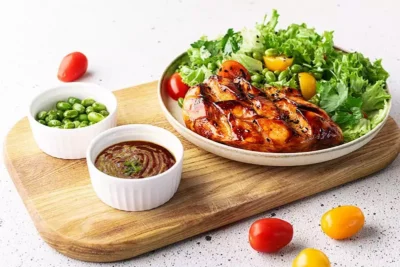 Grilled chicken with salad and dipping sauces, served on a wooden board for a delicious meal experience