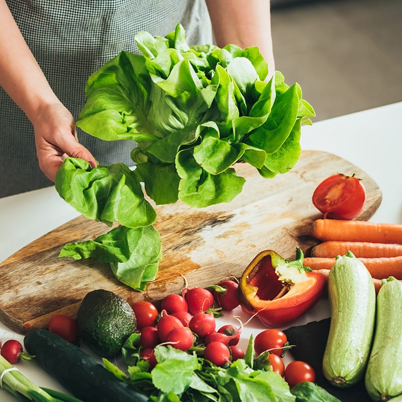 Woman preparing fresh lettuce and vegetables for healthy summer salads.