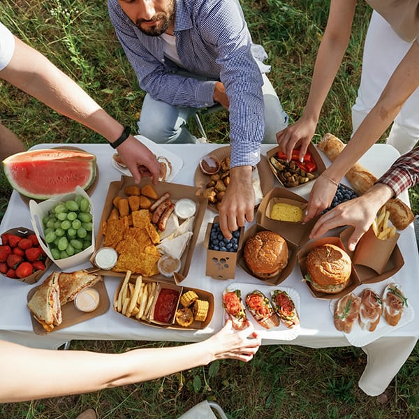 Friends enjoying outdoor summer gathering with healthy salads and picnic food on white table.