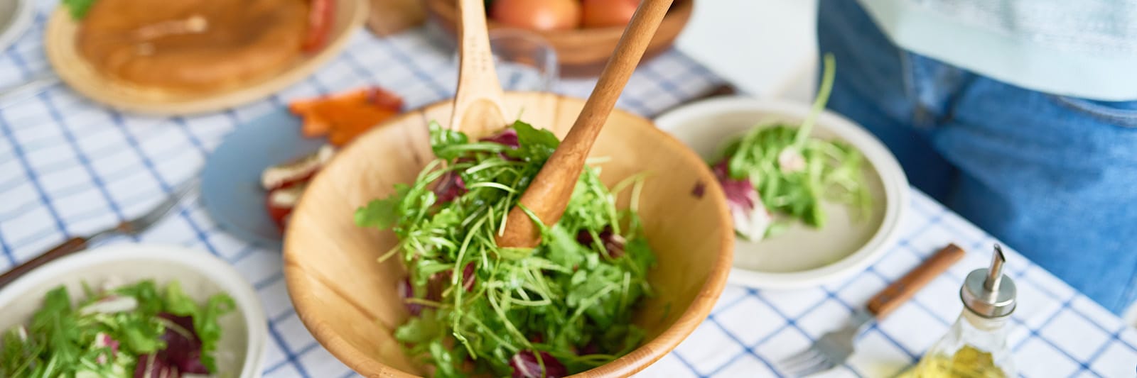 Woman tossing fresh green salad with wooden utensils in kitchen.